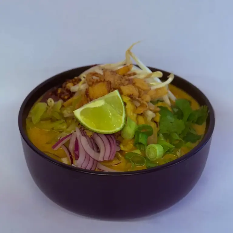 Bowl of khao soi curry noodle soup with crispy noodles and lime from Anchan Thai Fusion