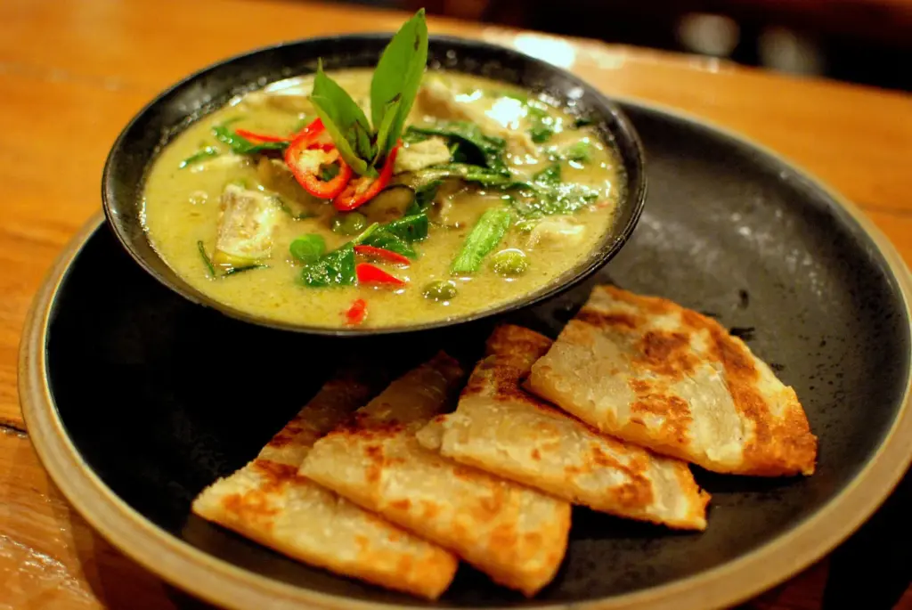 Bowl of Thai green chicken curry with red chili, served with pieces of roti