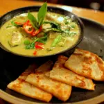 Bowl of Thai green chicken curry with red chili, served with pieces of roti