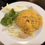 Pad thai wrapped in a lacy egg net, served with bean sprouts, chives and lime