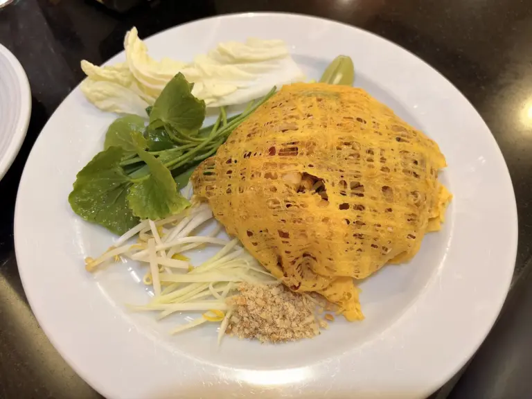 Pad thai wrapped in a lacy egg net, served with bean sprouts, chives and lime