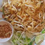 Plate of pad thai with crushed peanuts, bean sprouts and lime on the side