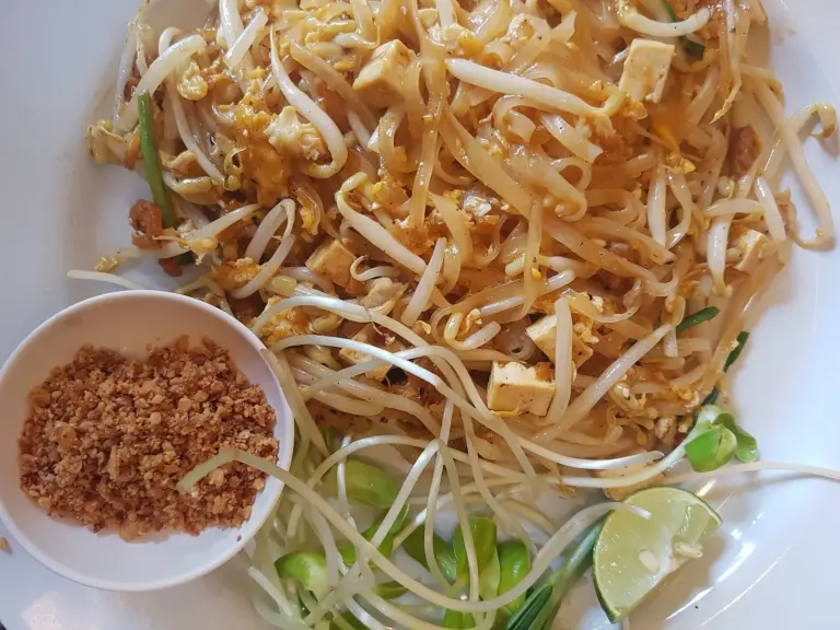 Plate of pad thai with crushed peanuts, bean sprouts and lime on the side