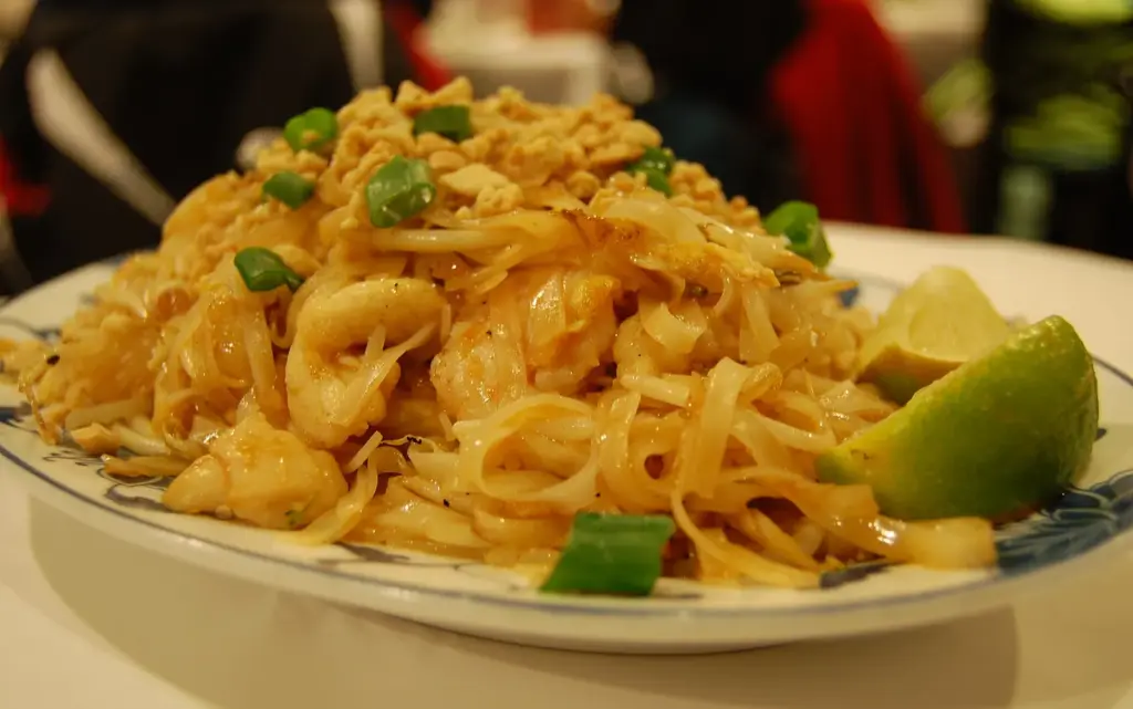 Mound of pad thai noodles with green onion and a wedge of lime