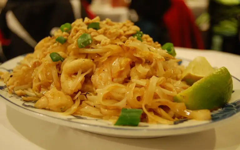 Mound of pad thai noodles with green onion and a wedge of lime