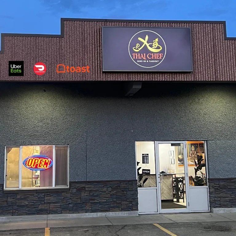 Thai Chef restaurant storefront at dusk with its lit sign and open door on Illinois Street in Fairbanks