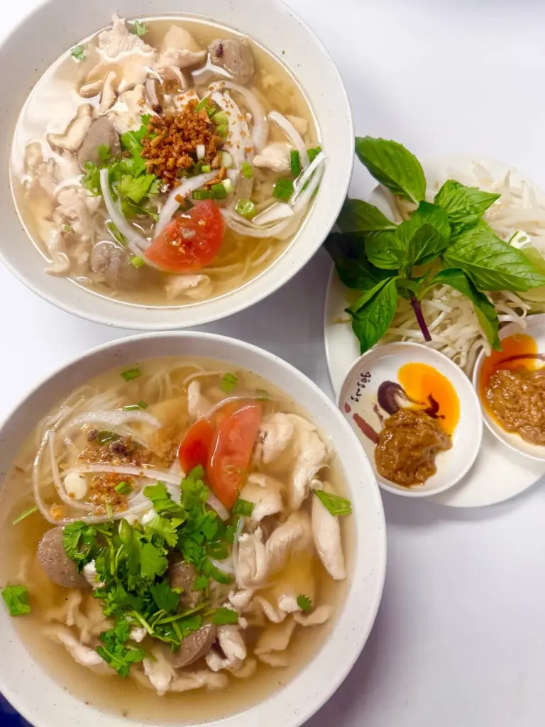 Two bowls of noodle soup with Thai basil, lime and condiments at Yes! Noodle Soup